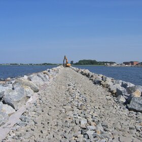 Rock embankment in the water with construction machinery in the background