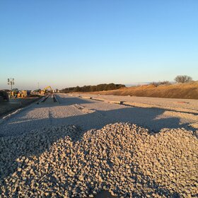 Large construction site with spread gravel surface, railway tracks and construction machinery