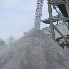 Pile of grey aggregate being formed with a conveyor system in the background