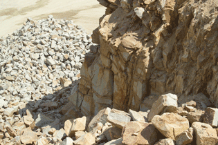 Close-up of a crusher system with rock material falling onto a pile