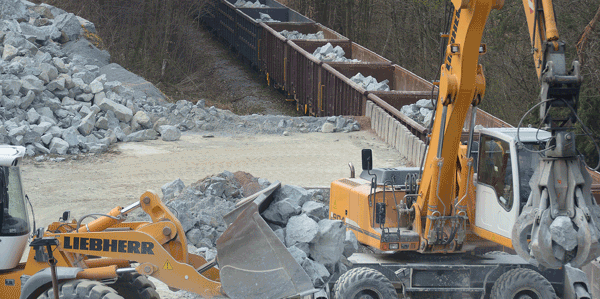 Wheel loader and excavator loading crushed stone into railway wagons