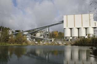 Quarry production facility with silos and conveyor belts next to a water pond