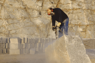 Worker splitting a massive stone block with a jackhammer in the quarry