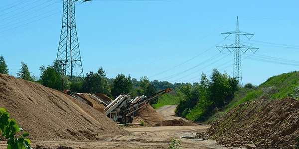 Open raw material extraction area with sand and soil piles and mobile screening equipment